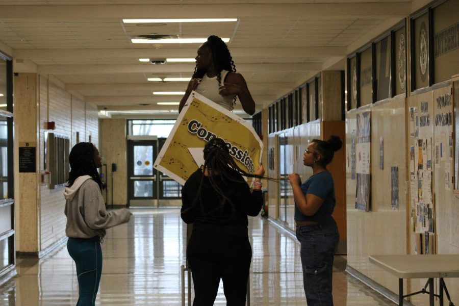 Grace Cannon, Audrey Ngamelue, Alera Blair, and Anorah wade help each other hang signs with directions for the school so the guests of Burke Bonanza can find their way.