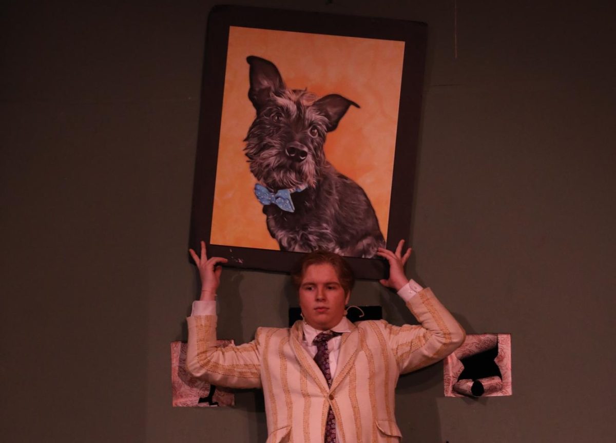 Eli Zagurski holds onto a falling painting in "The Play that Goes Wrong."